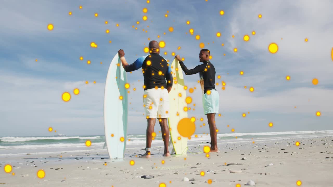 Senior and adult men with boards, camera sparking yellow dots growing over them preparing to surf