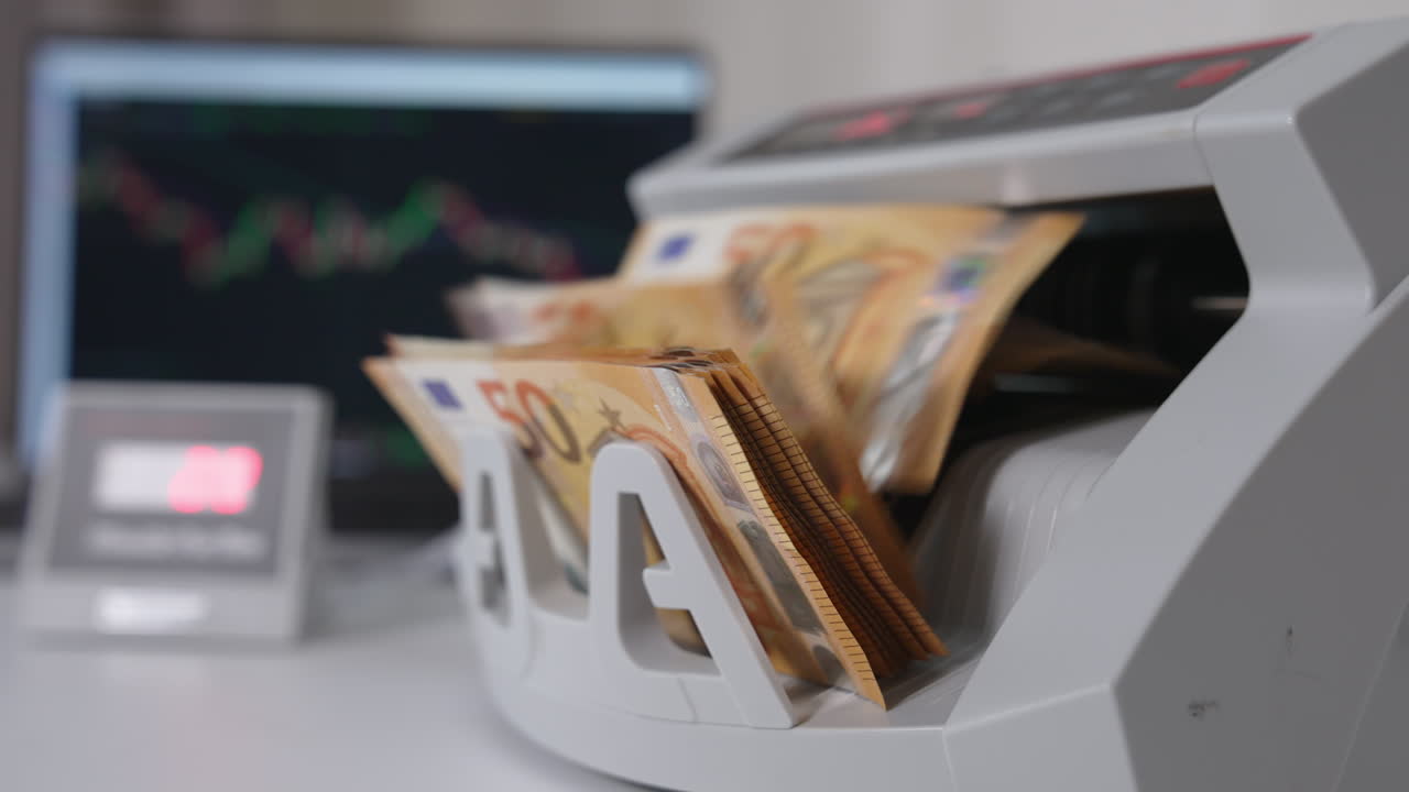 Working cash calculating equipment on the white table. Machine counting fifty euro banknotes. Laptop at backdrop.