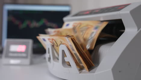working cash calculating equipment on the white table. machine counting fifty euro banknotes. laptop at backdrop.
