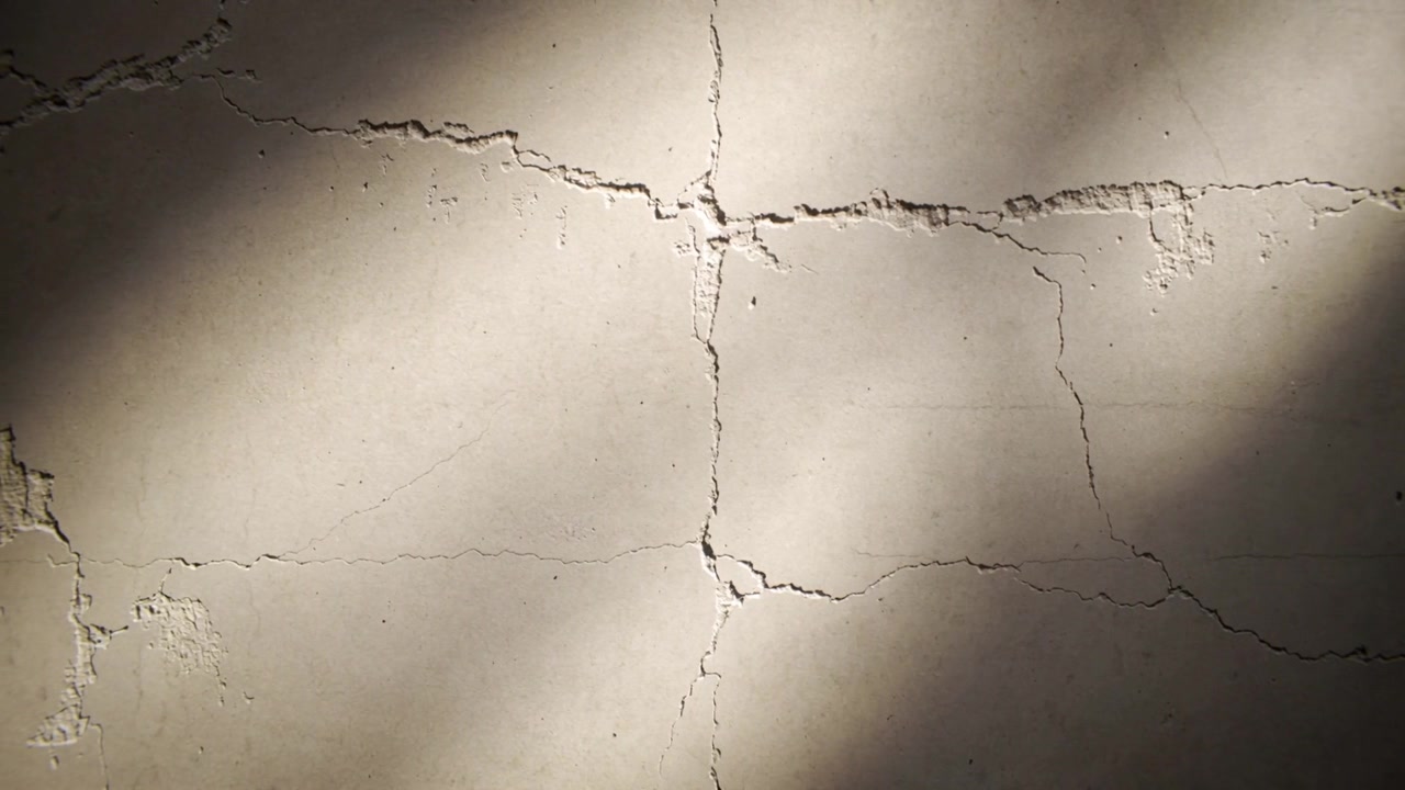 Shifting sunlight casting moving shadow patches across concrete wall, revealing crack grid