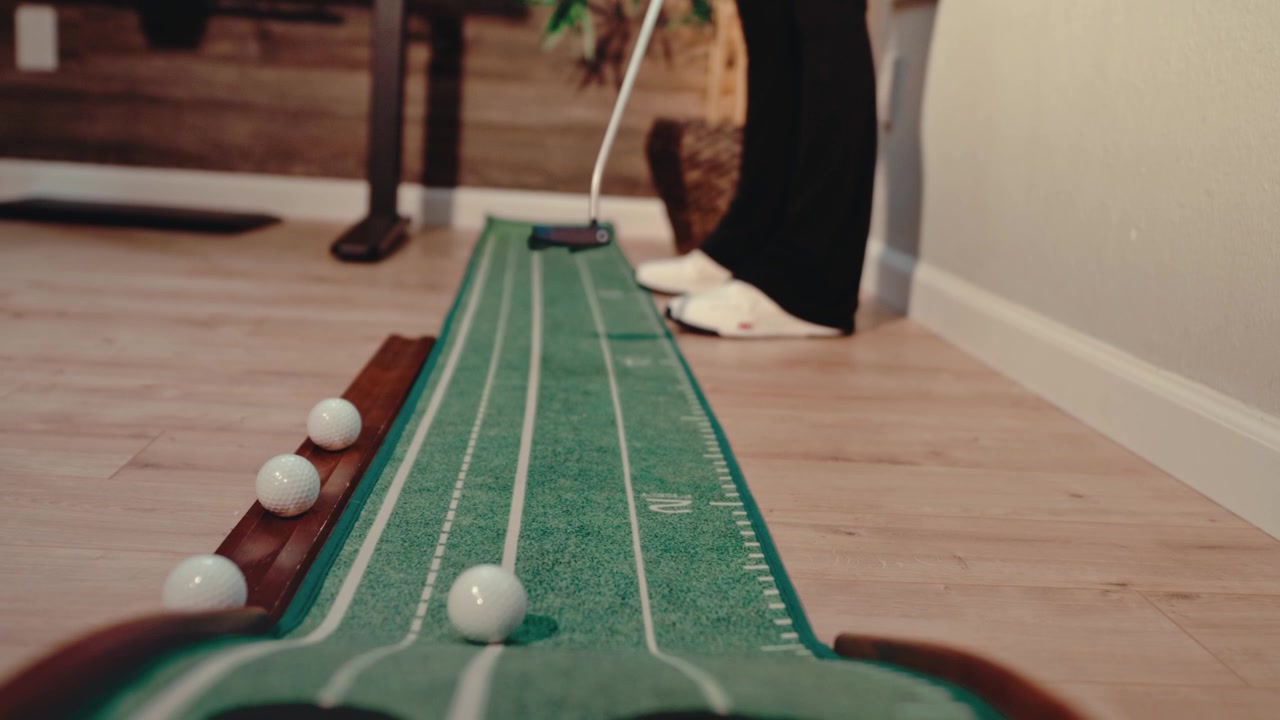 Un golfista si esercita su un tappeto da putting per interni nel suo ufficio domestico con più palline, ripresa dall'alto in 4K. Video di allenamento di golf, contenuti per la pratica a casa e annunci di prodotti.