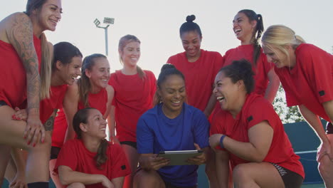 Female-Coach-Discussing-Tactics-With-Womens-Soccer-Team-Using-Digital-Tablet-Before-Match