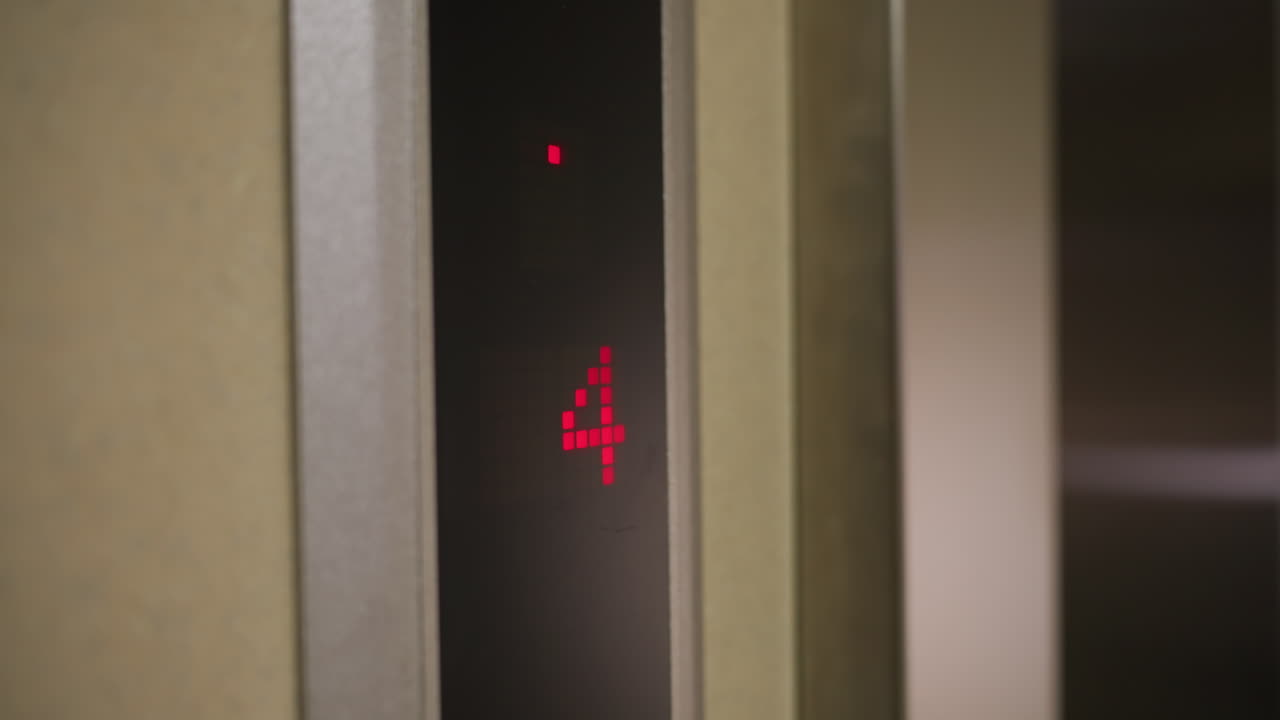 Elevator display showing downward arrow and floor 4, digital red indicator, modern elevator system, business building, corporate setting, elevator in motion, office environment