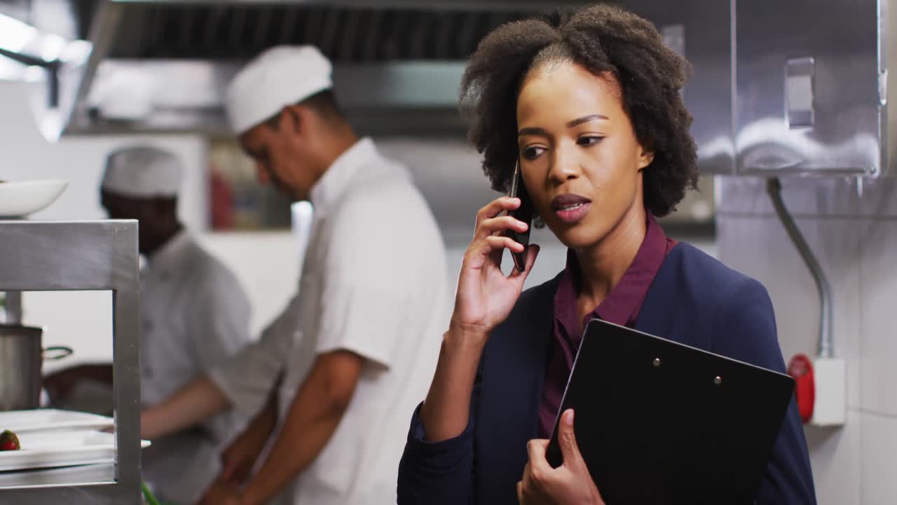 African american female manager talking on smartphone in restaurant kitchen