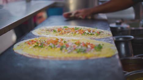 Primer-Plano-De-Dosa-Cocinando-Un-Plato-Del-Sur-De-La-India-Con-Puré-De-Patatas-Y-Verduras-En-Una-Sartén-De-Hierro-Plano-En-Un-Puesto-De-Comida-Callejera-En-La-India.