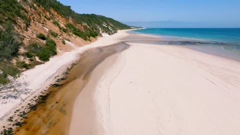 a river meets the ocean while the drone is revealing the endless pristine beaches of fraser island on a sunny day