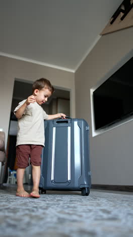 energetic kid runs into the room pulling a suitcase. low angle view at the toddler boy packing for vacation. low angle view. vertical video.
