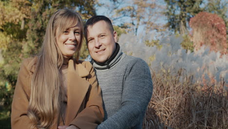 portrait of a young beautiful couple smiling and looking at the camera. standing in warm clothes in the autumn park