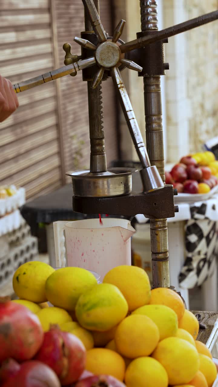 Succo di melograno che gocciola da un torchio manuale in metallo in una brocca presso un banco del mercato, primo piano verticale statico