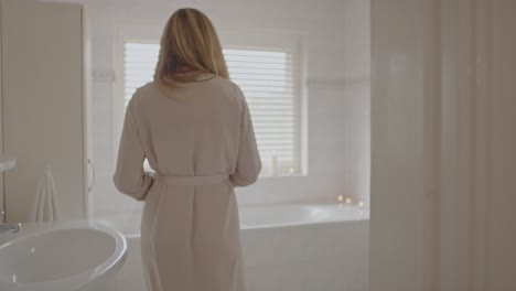 beautiful woman walking towards filled bathtub and opening her robe