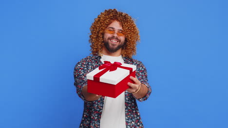 joven sonriente presentando regalo de cumpleaños caja de regalos extiende las manos promoción venta de descuento