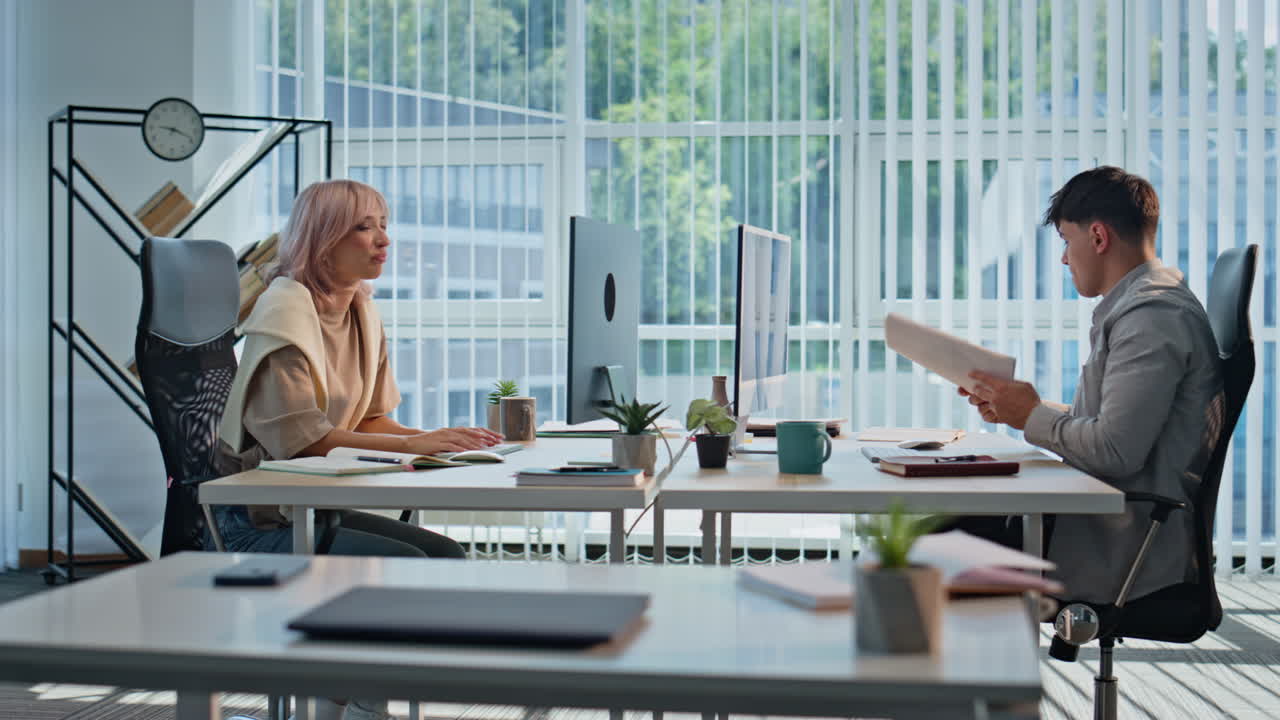 Woman giving papers colleague at panoramic office. Two coworkers communicating