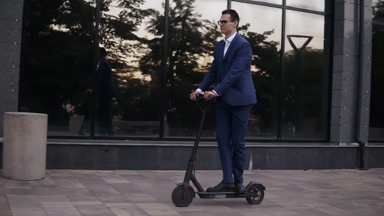 Young businessman in elegant blue suit and glasses riding and electric scooter for a business meeting in the office, office