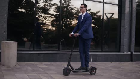 young businessman in elegant blue suit and glasses riding and electric scooter for a business meeting in the office, office