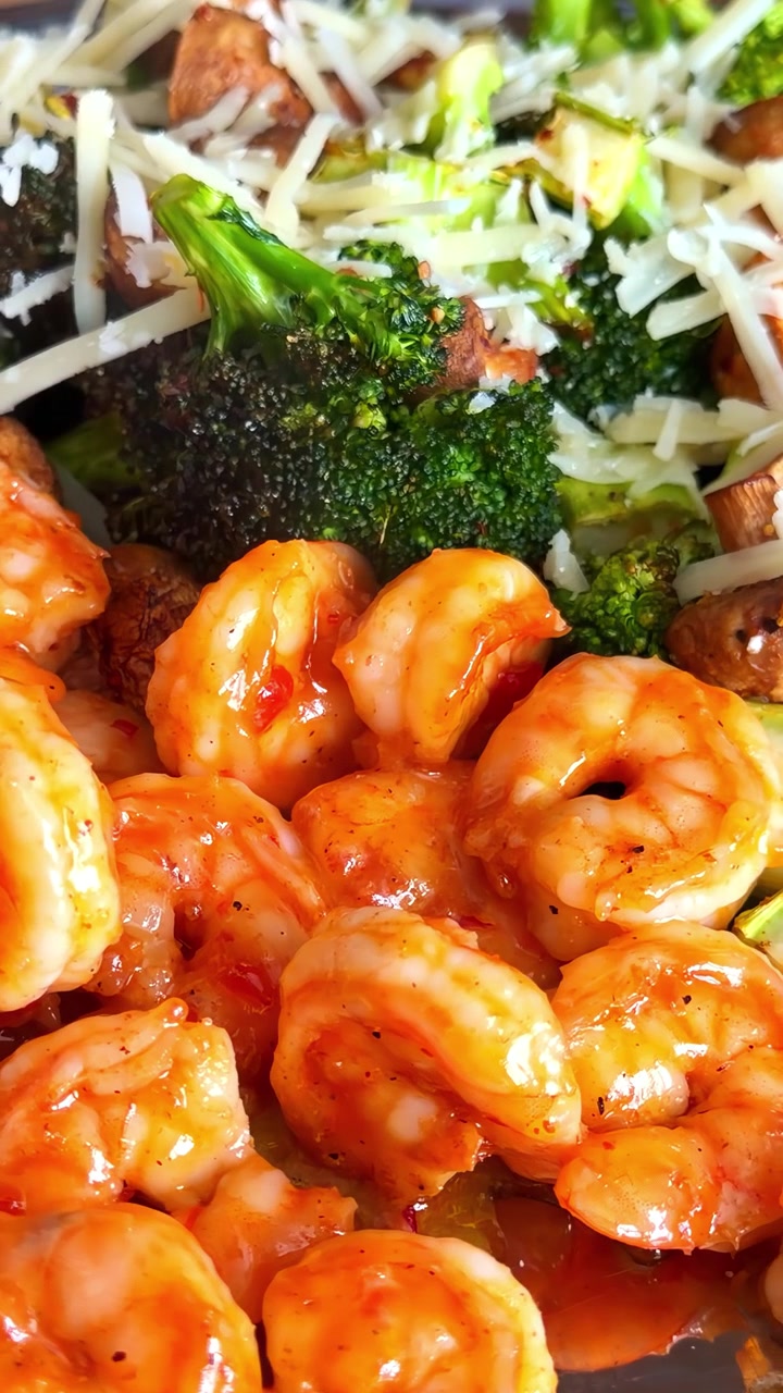 Primo piano estremo di succulenti gamberi al peperoncino e aglio serviti con broccoli freschi al vapore e formaggio Parmigiano. Ideale per contenuti culinari e di alimentazione sana