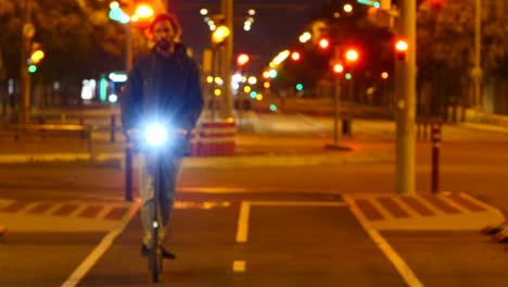 Mann-Auf-Elektroroller-Nähert-Sich-Nachts,-Rack-Fokus-Auf-Bokeh-Straßenlaternen