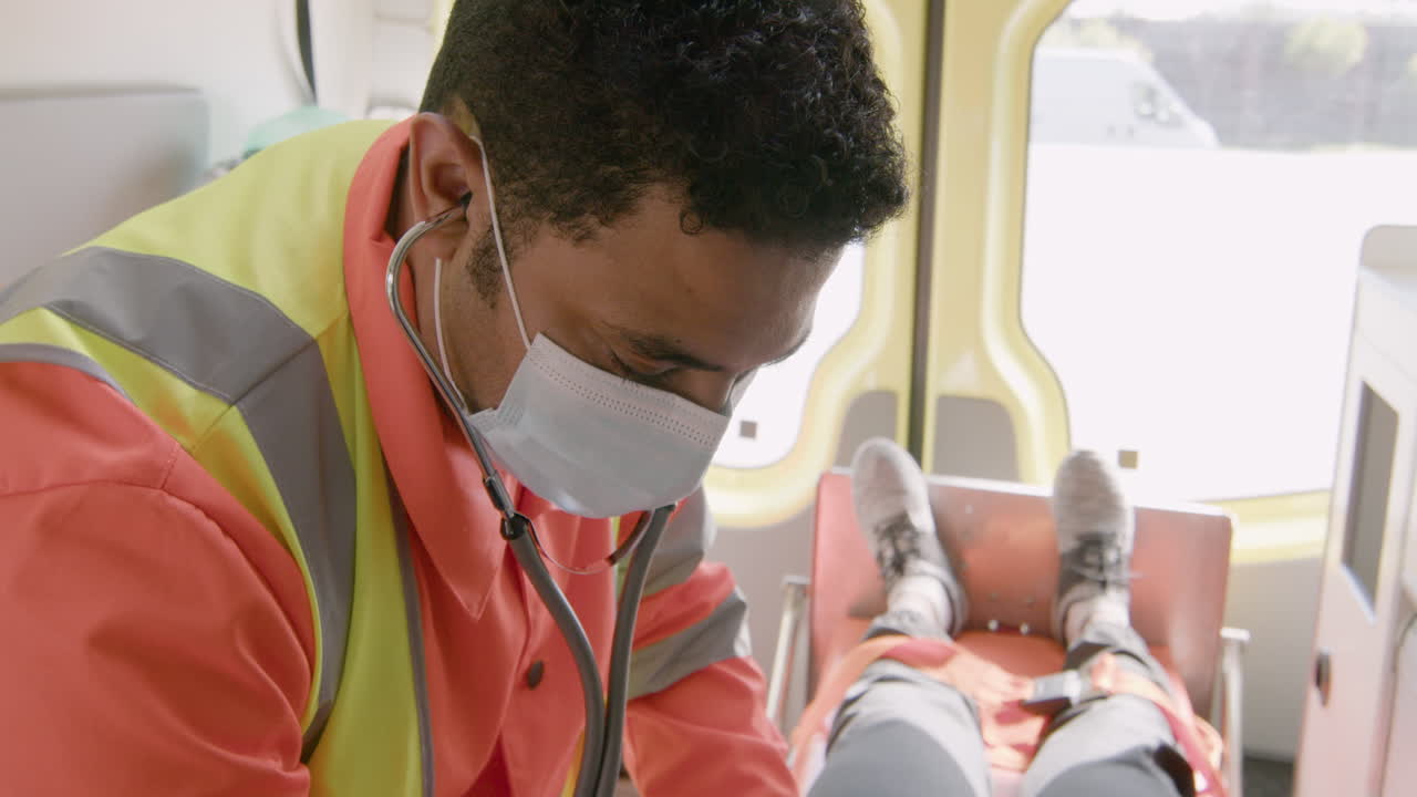 구급차 2에서 미국 환자에게 청진기를 사용하여 안면 마스크를 쓴 남성 구급대원