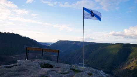 La-Bandera-De-Galicia-Sopla-Fuerte-En-El-Viento-Con-Vistas-A-La-Ribeira-Sacra-Y-Al-Cañón-Con-Un-Banco-Vacío