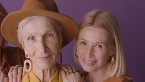 close up view of senior woman in hat and mustard shirt poses with two blonde mature women on purple background