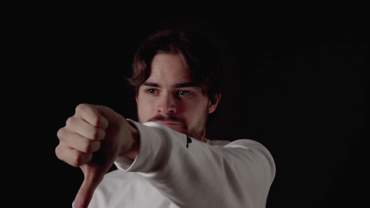 엄지손가락을 아래로 내리고, 반대하는 몸짓, 닫고, 검은 배경을 가진 세련된 청년