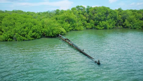 Toma-Aérea-De-Una-Tubería-Oxidada-Que-Corre-Hacia-Un-Lago-Rodeado-De-Manglares,-Vertiendo-Aguas-Residuales