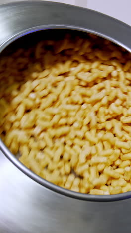 round metal tank with corn sticks being rotated at the factory automated production. sweet crispy snacks manufacturing. vertical video