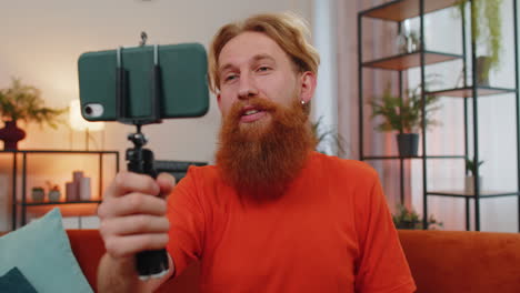 Bearded-man-blogge-taking-selfie-on-smartphone-communicating-video-call-home-online-with-subscribers