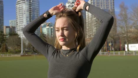 bella joven atando el cabello y estirándose antes de entrenar al aire libre