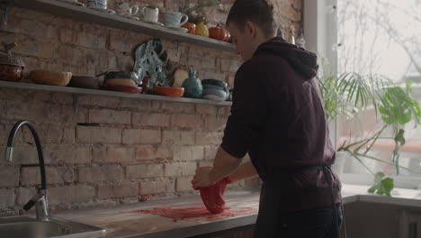 young man shaping red clay in a pottery studio kitchen