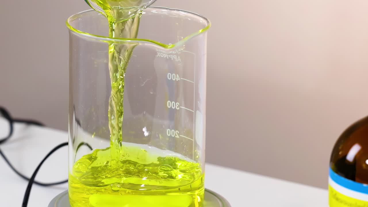 A sequence showing yellow liquid being poured into a beaker in a laboratory setting.