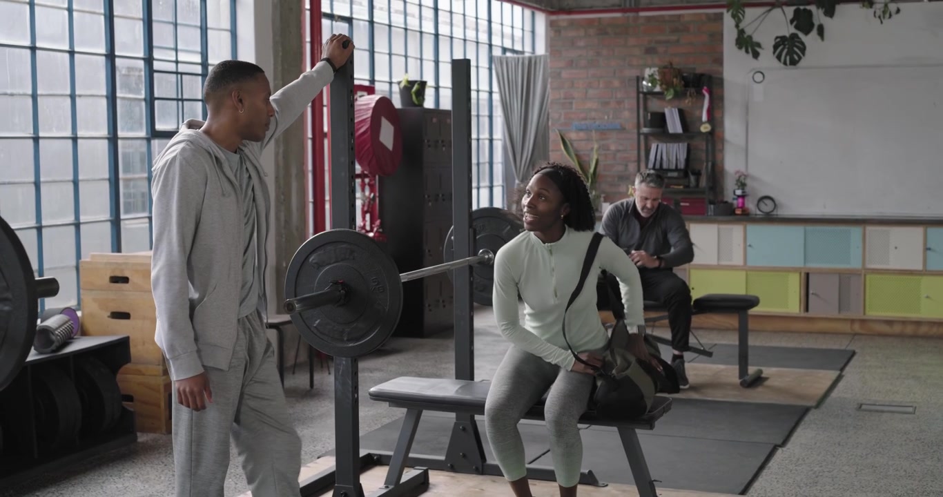 Afroamerikanskt par kramas efter att mannen kommit från gymmet, placerar träningsväskan på bänken och förbereder sig för träning.
