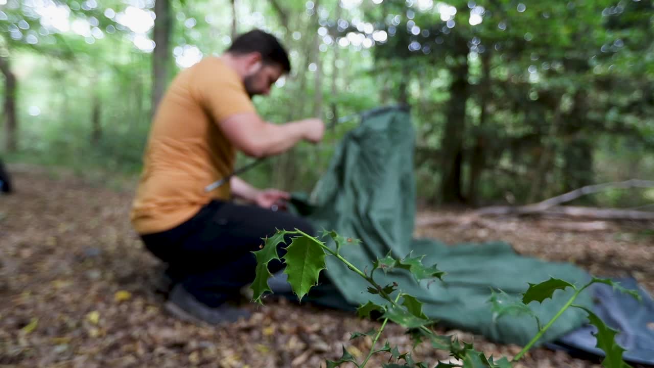 Blurred view of a man setting up camping tent at a campsite in the woods. Out-of-focus shot