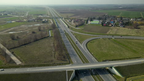 Vista-Aérea-De-La-Autopista-Road-S7-Cdry-Road-Y-El-Intercambio-De-Infinity-Road-Que-Revela-Un-Pequeño-Pueblo-Cerca-De-La-Carretera-En-Polonia
