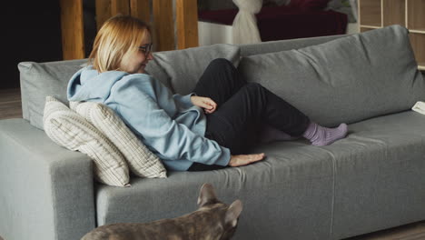 rear view of red haired woman caresses her bulldog dog while they are liying on the sofa in the living room at home