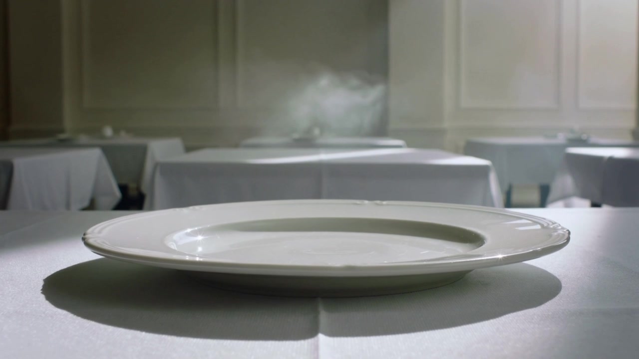 Vapore che appare e sale dietro un piatto da portata ovale bianco in una sala da pranzo formale, con tovaglia bianca.