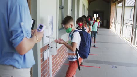 boy wearing face mask sanitizing his hands at school