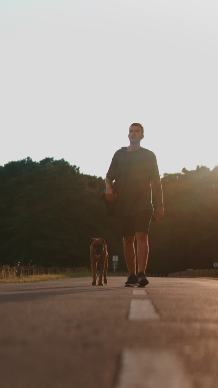 A man walking with his dog on a road at sunset