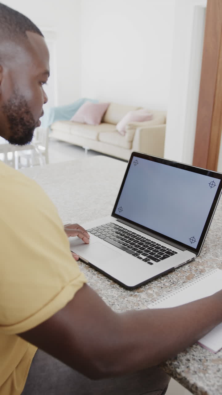 Vertical video of african american man using laptop with copy space on screen, in slow motion