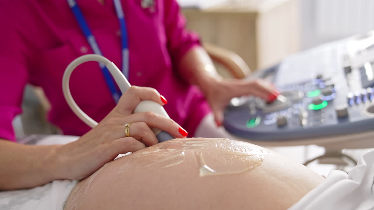 Pregnant woman doing ultrasound in clinic. Examination of baby at ultrasound. Doctor performing sonogram on belly in clinic. Process of fetus ultrasonography. Close-up.
