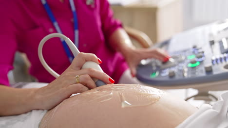 pregnant woman doing ultrasound in clinic. examination of baby at ultrasound. doctor performing sonogram on belly in clinic. process of fetus ultrasonography. close-up.