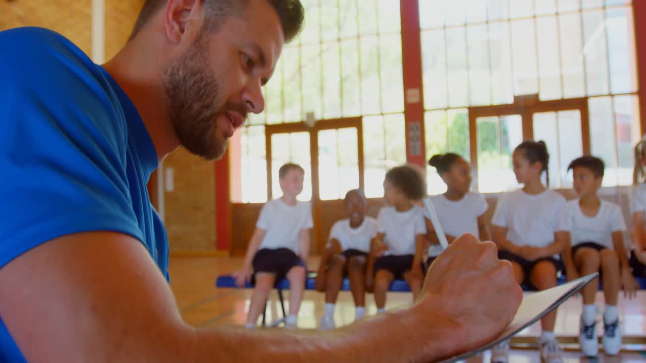 Caucasian basketball coach writing on clipboard in basketball court 4k