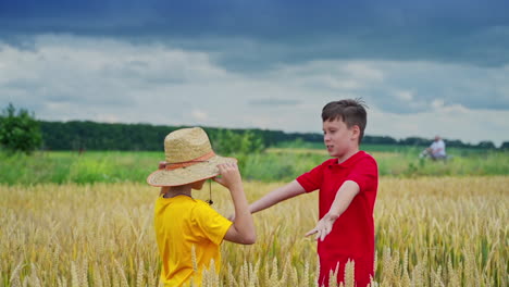 elder brother puts straw hat on younger kid head. video from the field. outdoor video. gold wheat and blue cloudy sky.