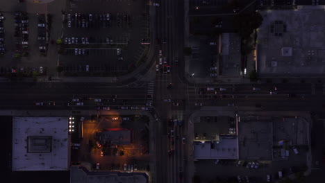 Dark-Road-intersection-at-dusk-with-car-traffic-passing-and-parking-lot-in-Los-Angeles,-California,-Rising-Aerial-Birds-Eye-Overhead-Top-Down-View