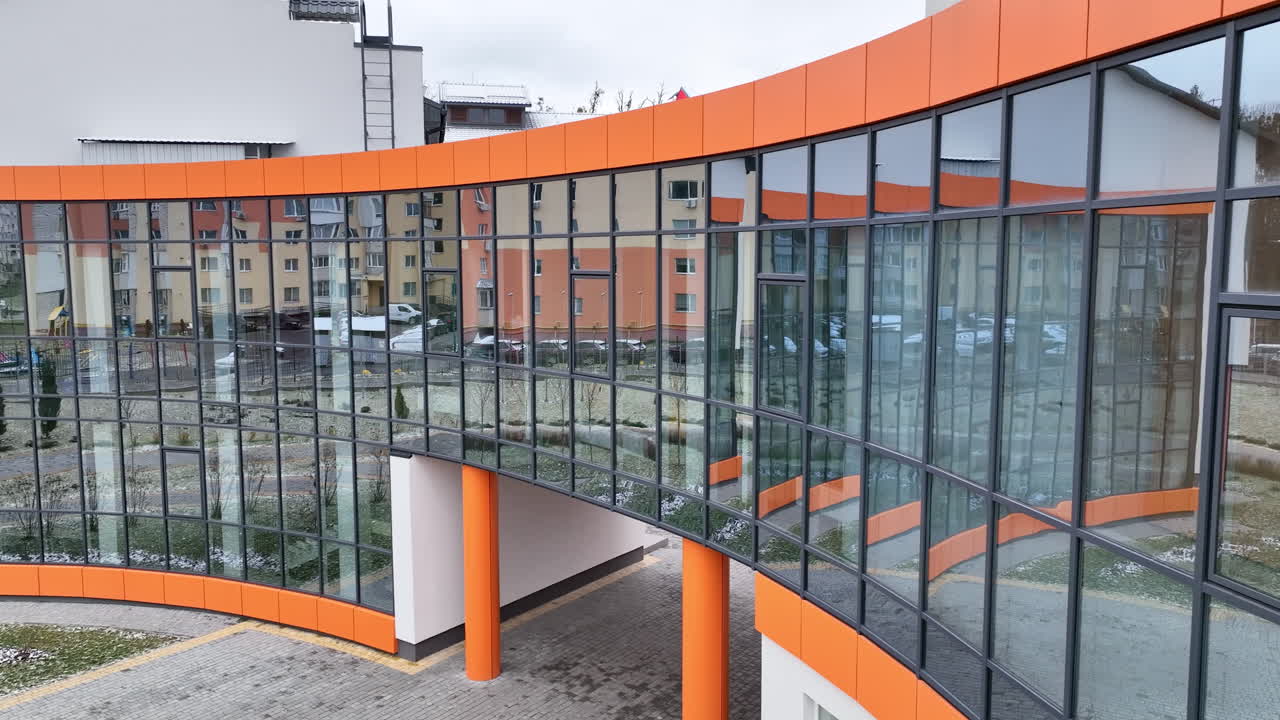 Front passage to the recently-built building with mirror windows and orange design elements. Blocks of flats reflecting in the mirrored windows.
