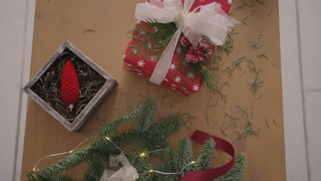 top-view-plan.-Fully-visible-the-table-with-the-decorations.-Female-hands-put-and-finalize-Christmas-gift-wrapped-in-craftool-paper-on-a-wooden-table.-Bandaging-tape-and-tied-bow.