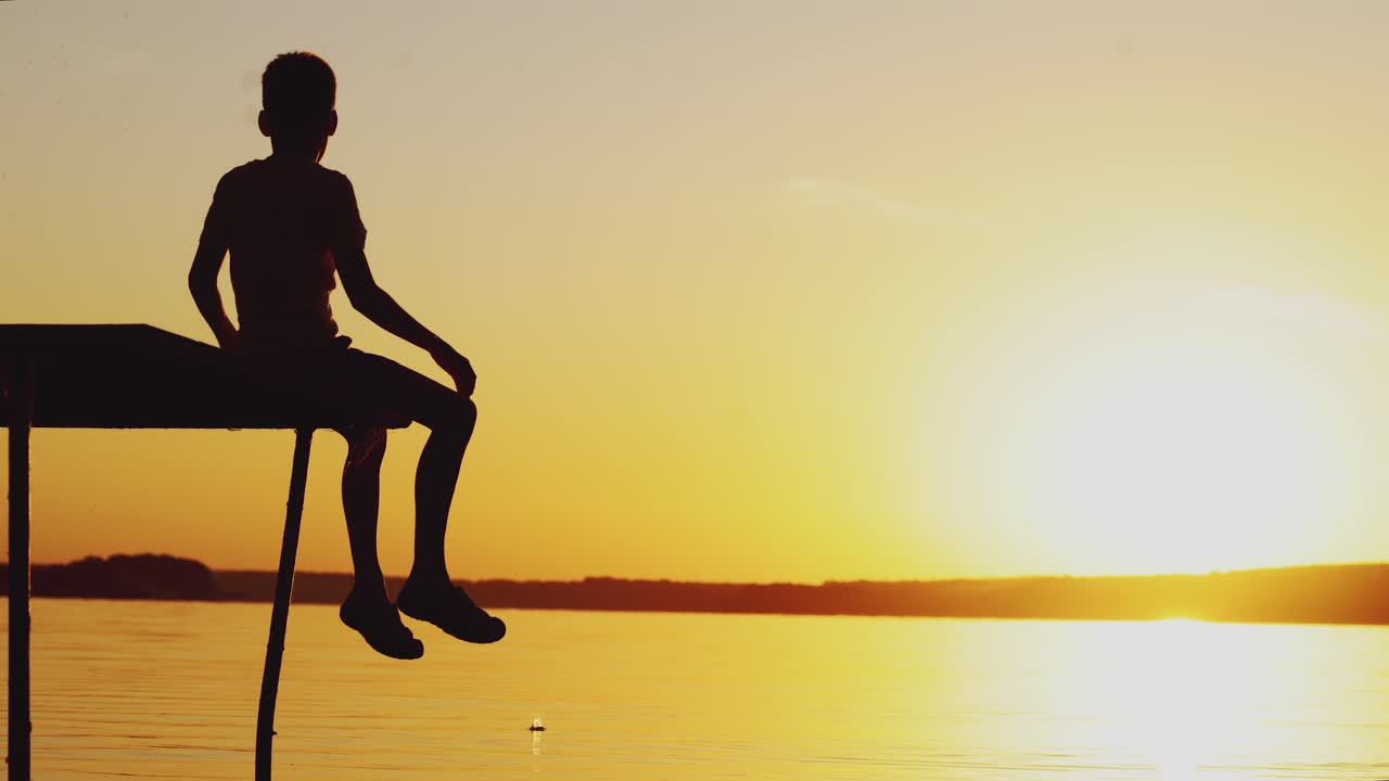 Silhouette of a boy playing on an old bridge by the river. Beautiful summer sunset