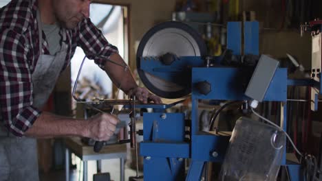 midsection of caucasian male knife maker in workshop using saw