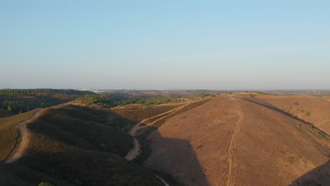 Toma-Aérea-Hacia-Adelante-De-Hermosas-Colinas-áridas-Y-Secas-Y-Senderos-De-Tierra-Con-La-Ciudad-De-Portimão-En-La-Distancia-En-Algarve,-Portugal