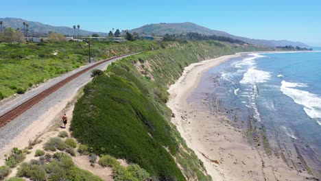 Aerial-Over-Man-Walking-On-Railroad-Tracks-Above-The-Pacific-Coast-Near-Carpinteria-Bluffs-Santa-Barbara-California-1