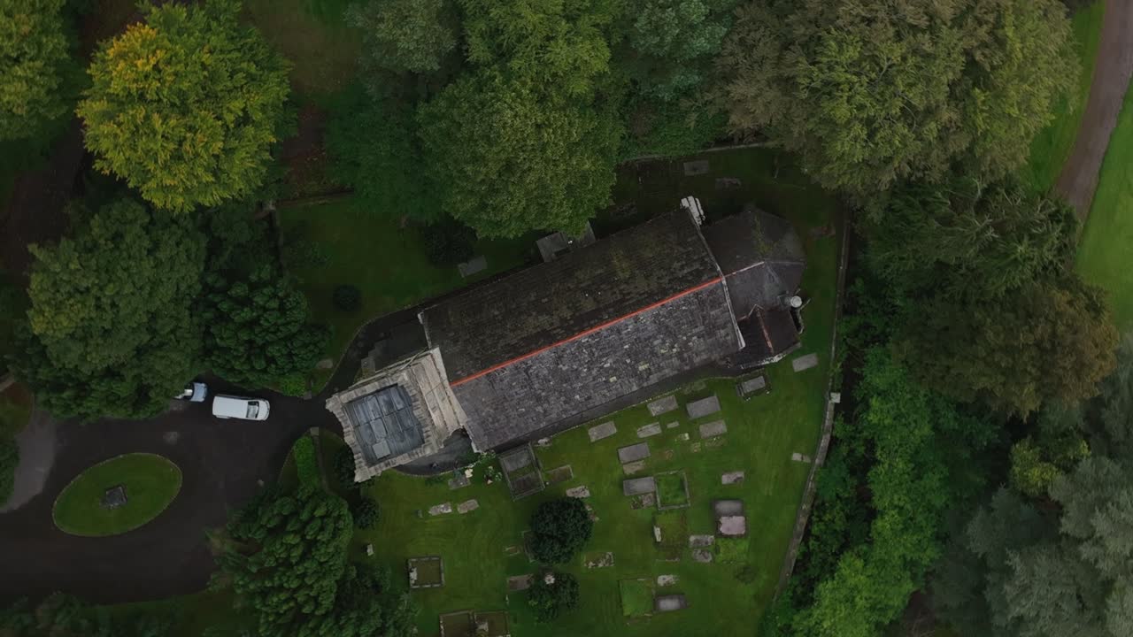 St. Salvator's Church, Glaslough, County Monaghan, Ireland, September 2022. Drone top down orbit ascend above weathered church rooftop in middle of trees.